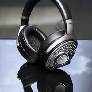 Close-up of black over-ear headphones with a perforated silver grille resting on a reflective surface.
