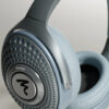 Over-ear light blue headphones close-up showing perforated ear cup and brand logo on the metallic plate.